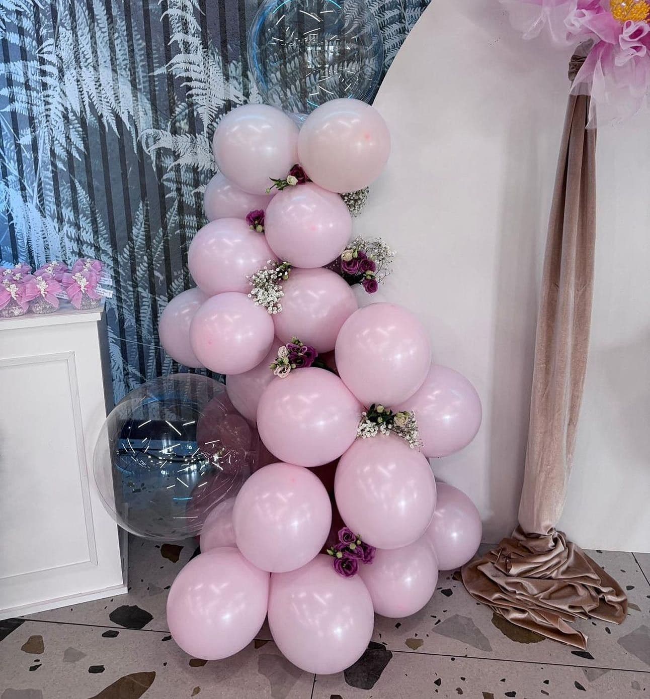 Colonna di palloncini rosa con fiori davanti a un fondale bianco